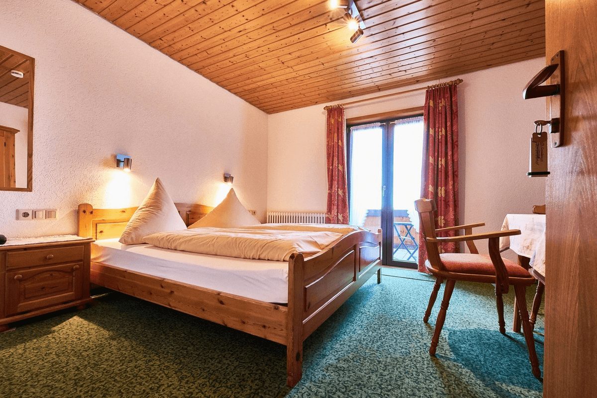 Doppelzimmer mit Balkontür, Nachttischlampen und Sitzgelegenheit